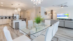 A modern kitchen with white cabinets, a stainless steel refrigerator, and a glass dining table with white chairs.