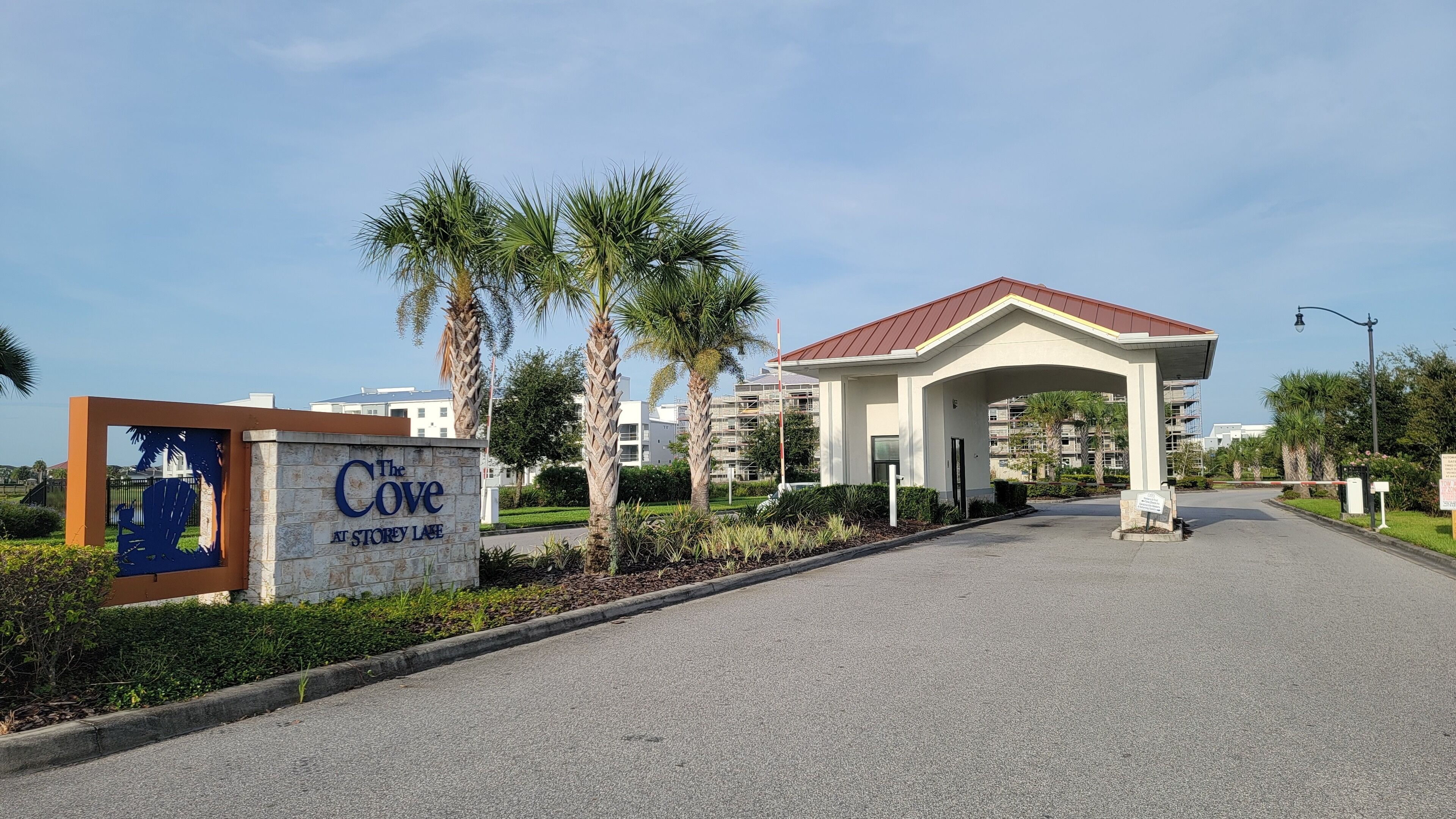 A gated entrance to The Cove at Storey Lake, featuring a clear pathway, palm trees, and a building with a red roof.