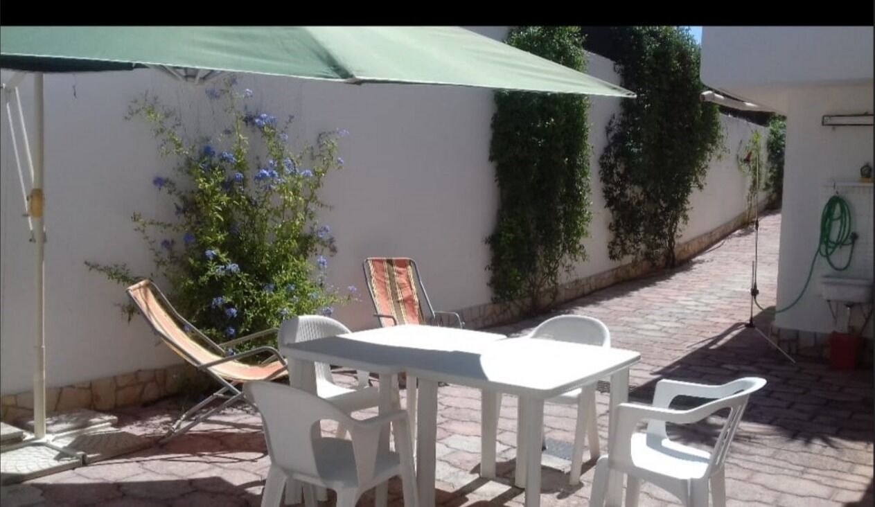 An outdoor patio with a white table and chairs, a green umbrella, and a wall with climbing plants.