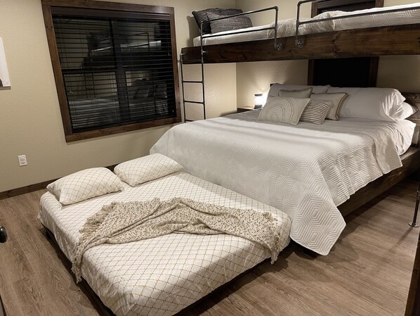 Habitación con literas, una litera inferior, cama con ropa de cama estampada, ventana con persianas y suelo de madera.