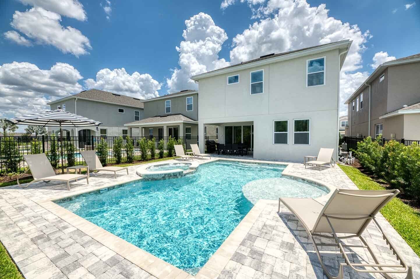 Un moderno edificio residencial con piscina, mobiliario exterior y un jardín cuidado.