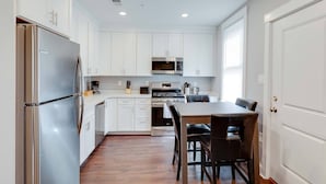 A compact kitchen with white cabinets, stainless steel appliances, and a dining area with a wooden table and chairs. - 3 Bed 2 Bath Tourist House near Kendall Square (Cambridge)