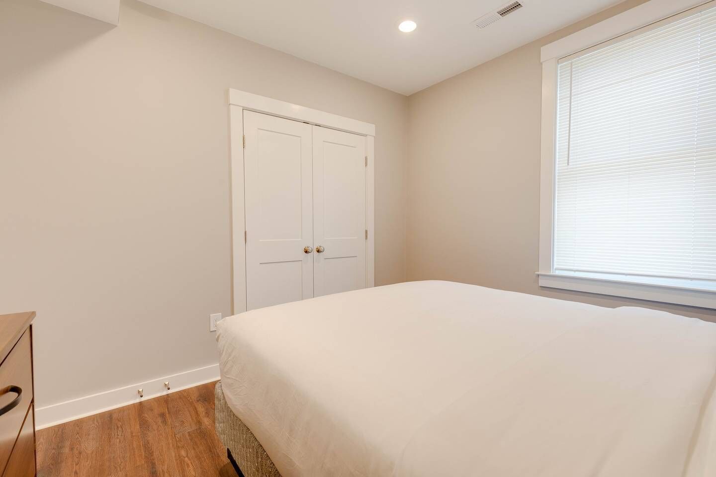 A bedroom with a bed, a wardrobe, a window with blinds, and a wooden floor.