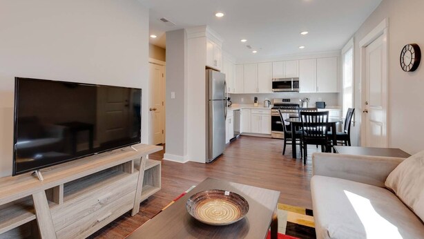 A modern living room with a flat-screen TV, wooden entertainment unit, and a dining area with a table and chairs. - 3 Bed 2 Bath Tourist House near Kendall Square (Cambridge)