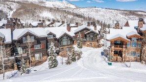A snow-covered lodge with multiple wooden buildings, a ski trail, and a mountainous backdrop. - Deer Valley luxury mountainside escape, outdoor seating, private hot tub, walk to hiking trails (Park City)