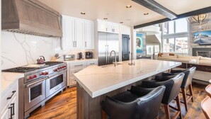 A modern kitchen with white cabinetry, stainless steel appliances, and a large island with bar stools. - Deer Valley luxury mountainside escape, outdoor seating, private hot tub, walk to hiking trails (Park City)