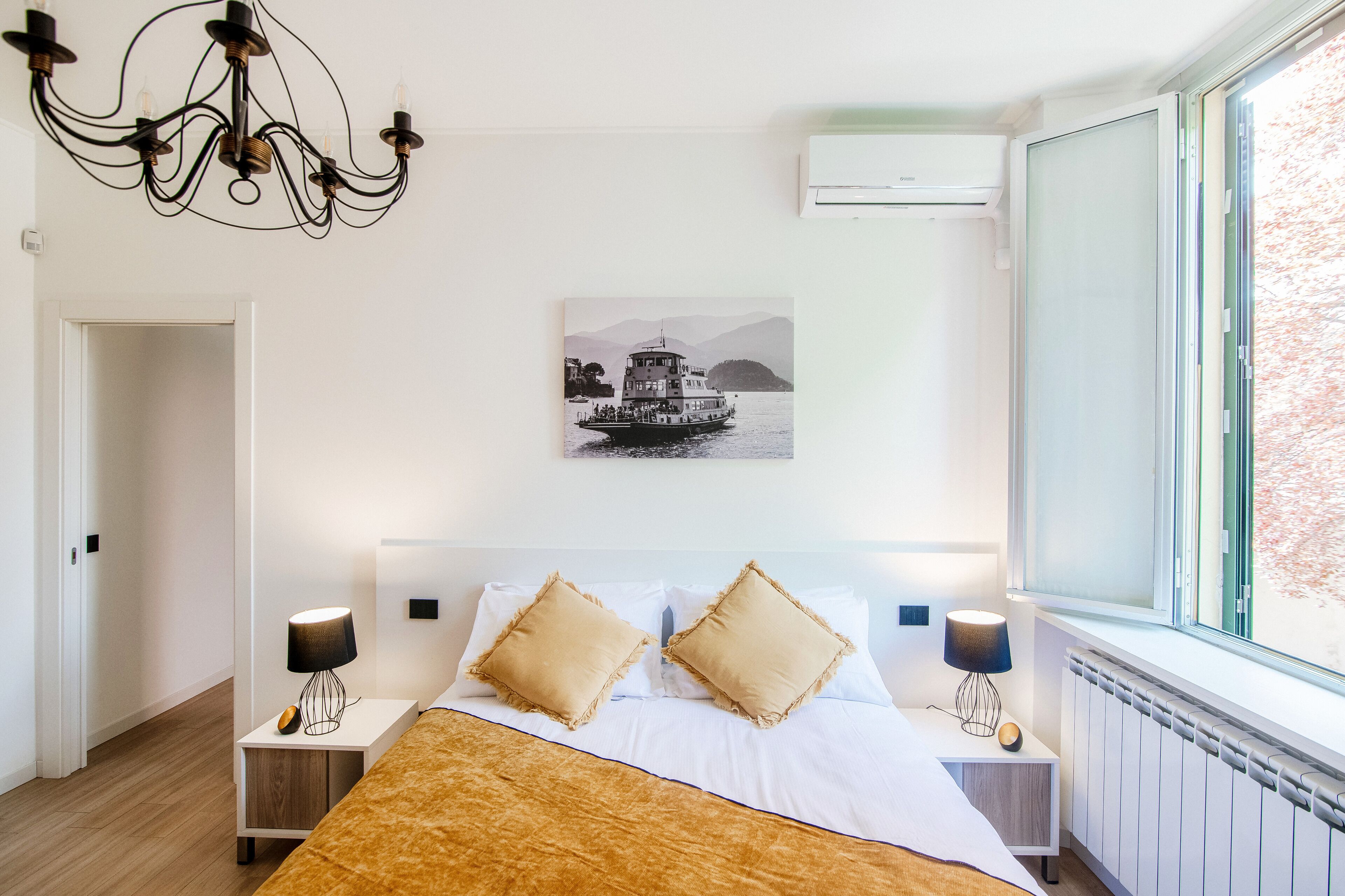 Una camera da letto con un letto, due comodini, un lampadario, una finestra e un condizionatore d'aria a parete.