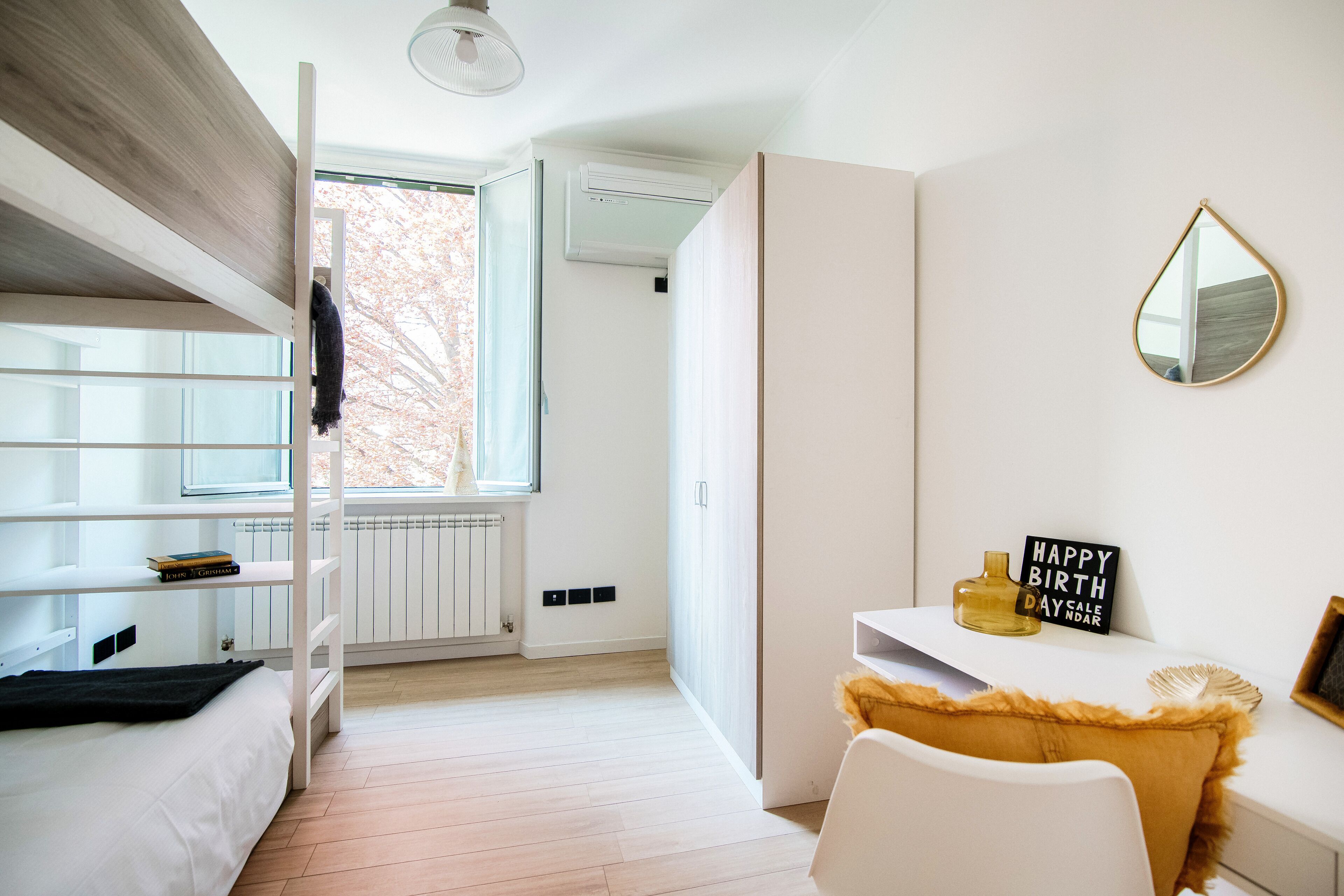 Un dormitorio moderno con literas, un escritorio, una silla, un espejo y una ventana.