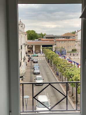 A street view from a window overlooking a road lined with parked cars and trees, with buildings and a bridge in the background. - Résidence Gaby & Tom (Contrexéville)