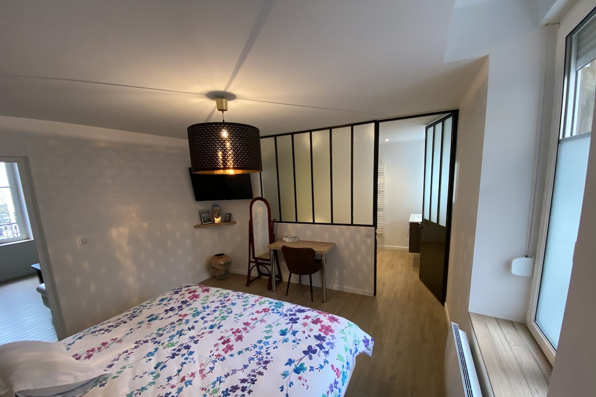 A modern bedroom with a bed, a desk, and a chair. There is a large window and a ceiling light fixture.