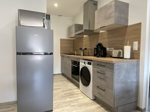 A compact kitchen with a stainless steel refrigerator, a washing machine, and a coffee maker. - Résidence Gaby & Tom (Contrexéville)