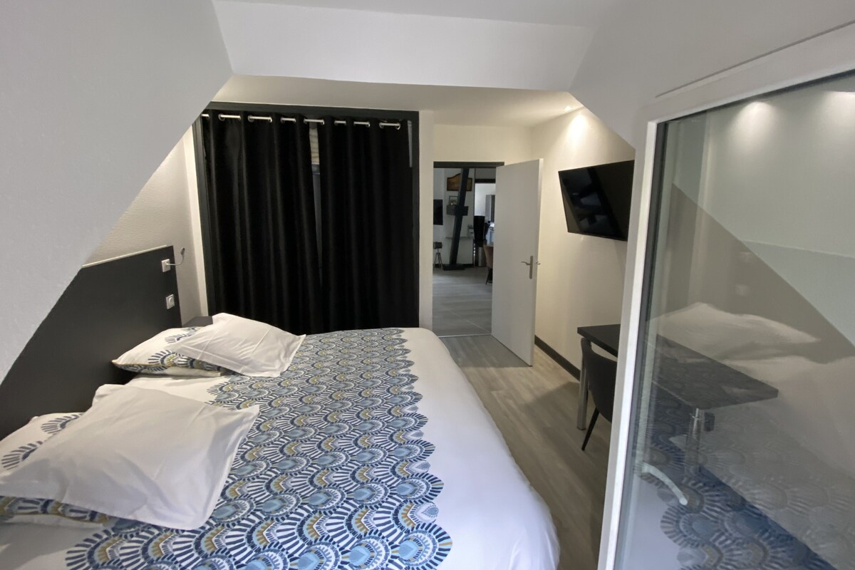 A modern hotel room with a bed, a desk, a TV, and a sliding door leading to a bathroom.
