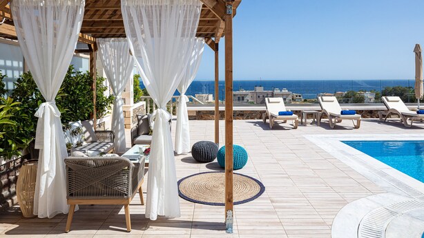Ein Poolbereich auf dem Dach mit Liegestühlen, einer Pergola mit weißen Vorhängen und Blick auf das Meer.