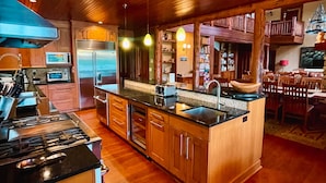 Una cocina amplia con armarios de madera, una isla central y un comedor con techo alto y vigas de madera.