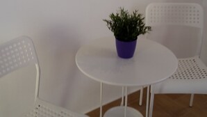 Een kleine witte tafel met een paarse bloempot met groene planten, omringd door twee witte stoelen met geperforeerde rugleuningen.