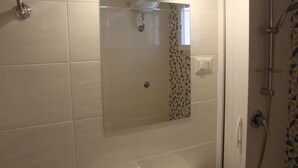 Een badkamer met een glazen douchecabine, een zichtbare stopcontact en een betegelde spatwand met een patroon.