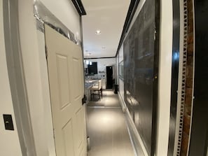 A narrow hallway with a kitchen area at the end, featuring a countertop and chairs. - The Blackberry Tree House (Camden)