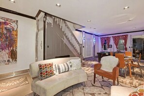 A modern living room with a sofa, a chair, a staircase, and a dining area with chairs and a table. - The Blackberry Tree House (Camden)