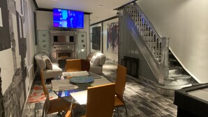 A modern living room with a glass dining table, comfortable seating, a fireplace, a television, and a staircase. - The Blackberry Tree House (Camden)
