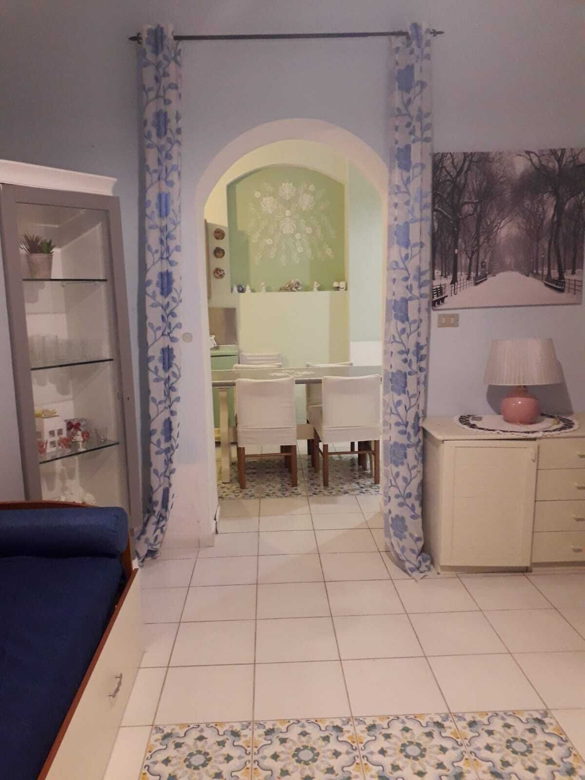 A room with a bed, a desk, and a chair. There is a cabinet with a lamp on top.