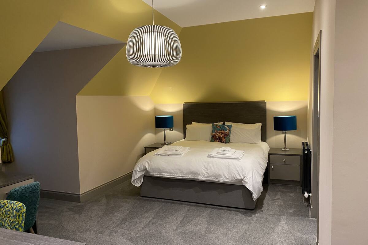 Ein modernes Schlafzimmer mit einem Bett, zwei Nachttischen, einer Hängelampe und Blick ins Freie.