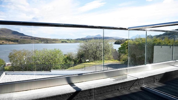 A modern balcony with a glass railing overlooking a lake and mountains. - Taransay House (Portree)