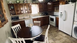 Une cuisine avec des meubles de rangement en bois, une table à manger avec des chaises, un réfrigérateur et un ventilateur de plafond.