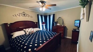Une chambre à coucher comprenant un lit, un ventilateur de plafond, une commode, un miroir et un téléviseur.