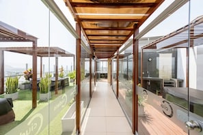 A modern rooftop terrace with glass railings, potted plants, and outdoor seating.