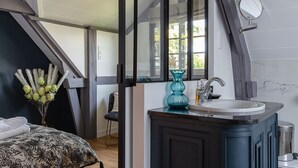 A bedroom with a bed, a window, a mirror, and a bathroom with a sink and a vase. - L'Atelier de La Maison Saint Léonard | pretty shared garden honfleur center (Honfleur)