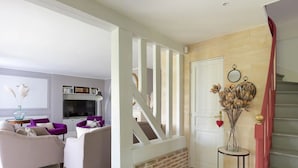 Un salon avec une cheminée, un escalier et une porte ornée d’un miroir et d’objets décoratifs.
