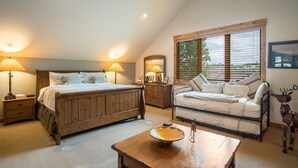 Een slaapkamer met een groot bed, een bank, een houten tafel en een raam met zonwering.