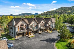 Une rangée de bâtiments de style chalet, dotés de nombreux balcons, et un espace de stationnement situé à l’avant.
