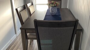 Un comedor con mesa y sillas de madera, un jarrón con flores y vistas al exterior a través de una ventana.