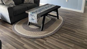 Una sala de estar con un sofá gris oscuro, una mesa de centro estampada y un televisor montado en la pared.