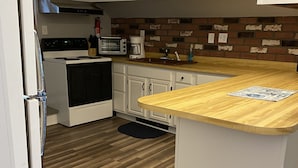 Una cocina con encimera de madera, armarios blancos, microondas, estufa y salpicadero de ladrillo.