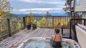 A hot tub on a wooden deck with a view of a forest and mountains. - Entire Suite,Ocean,mountain view,jacuzzi in the Suite,next to Mount Maxwell park (Salt Spring Island)