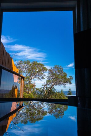 Udsigt gennem et vindue, hvor et træ og himlen klart reflekteres.