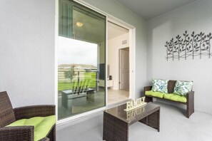 A balcony with wicker furniture, a glass door leading to a room, and a wall art piece.