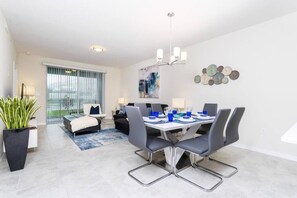 Ein modernes Wohnzimmer mit Essbereich, großen Fenstern und einem dekorativen Wandbild.