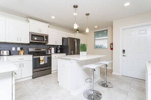 A modern kitchen with white cabinets, stainless steel appliances, and a central island with bar stools. - Lovely Storey Lake Brand New Apt 3111 ( Free Water Park!!!) (Kissimmee)