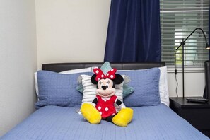 A bed with a plush Minnie Mouse toy, blue bedding, and a nightstand with a lamp.