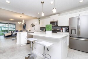 Una cocina moderna con armarios blancos, electrodomésticos de acero inoxidable y una isla central con taburetes de bar.