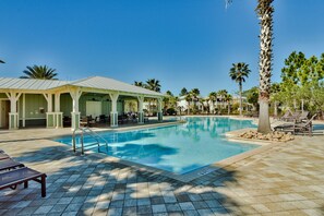 Un área de piscina con zona de estar cubierta, sillas de descanso y una palmera.