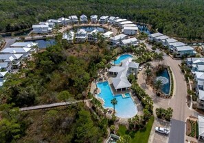 Vista aérea de un complejo turístico con varias construcciones, una piscina central y abundante vegetación circundante.