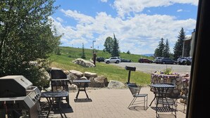 Un espace extérieur aménagé en terrasse, avec un barbecue, des chaises et des tables en métal, le tout entouré de rochers et de verdure.