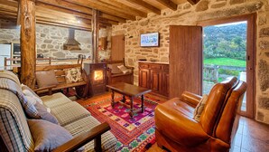 A cozy cabin interior with a stone wall, wooden furniture, a fireplace, and a view of the outdoors.