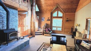 A cozy cabin interior with a stone fireplace, wooden walls, a staircase, and a leather sofa.