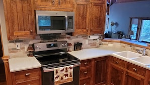 A kitchen with wooden cabinets, a stainless steel microwave, a stove, and a sink.