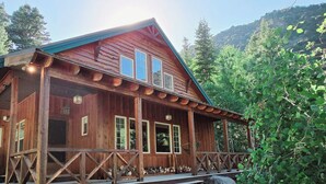 A wooden cabin with a porch, large windows, and a staircase leading up to the entrance.